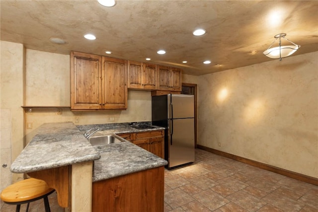 kitchen with freestanding refrigerator, a sink, a kitchen bar, black electric cooktop, and brown cabinets