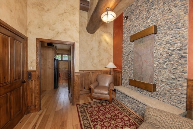 living area with a wainscoted wall, a high ceiling, and light wood finished floors