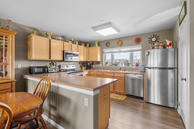 kitchen with appliances with stainless steel finishes, light brown cabinetry, kitchen peninsula, and sink