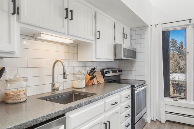 kitchen with sink, white cabinets, stainless steel appliances, light stone countertops, and a baseboard heating unit