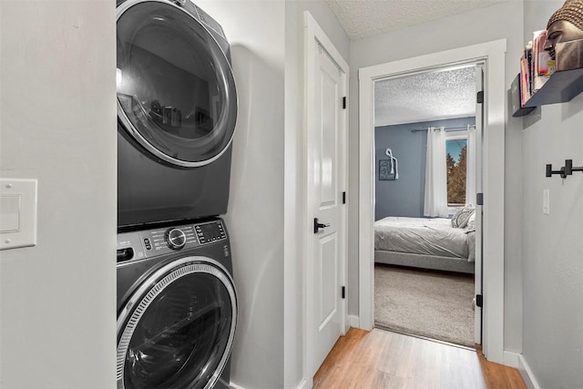 clothes washing area with light hardwood / wood-style flooring, stacked washer and clothes dryer, and a textured ceiling