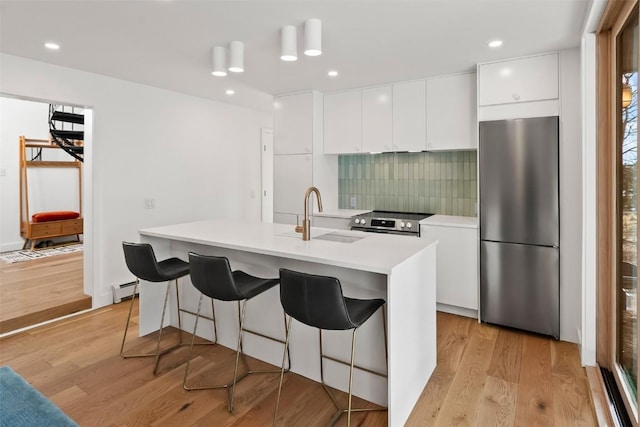 kitchen with appliances with stainless steel finishes, tasteful backsplash, sink, white cabinets, and an island with sink