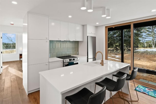 kitchen featuring stainless steel appliances, a kitchen island with sink, sink, light hardwood / wood-style floors, and white cabinetry