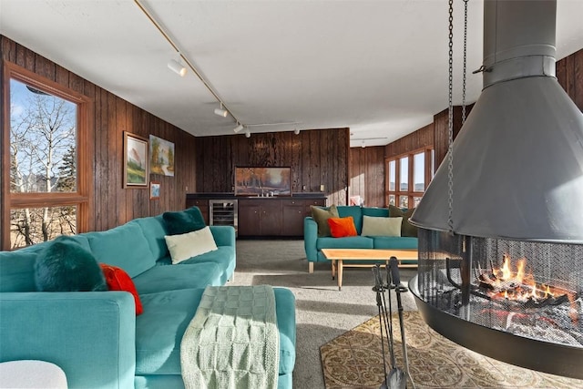 living room featuring carpet flooring, wooden walls, rail lighting, and wine cooler