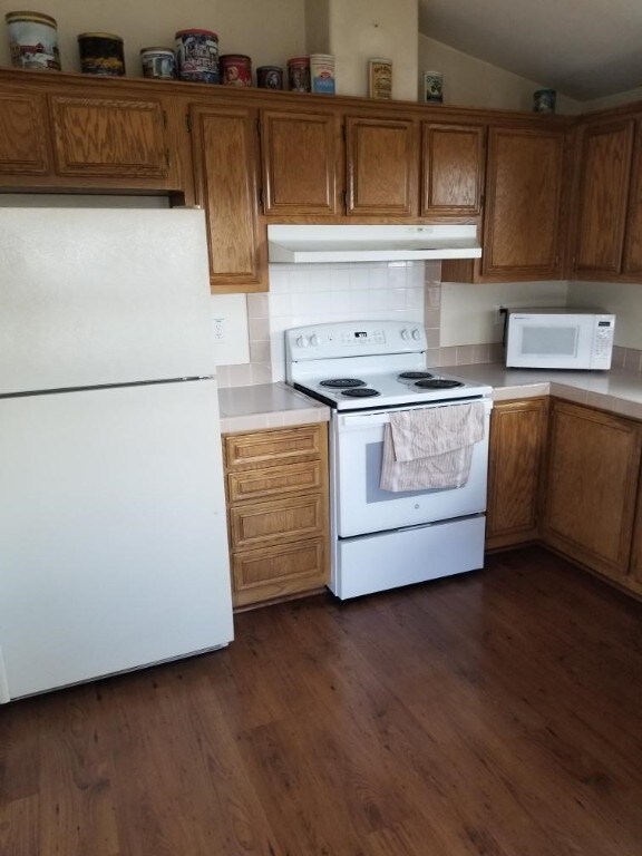 kitchen with lofted ceiling, decorative backsplash, white appliances, and dark wood-type flooring