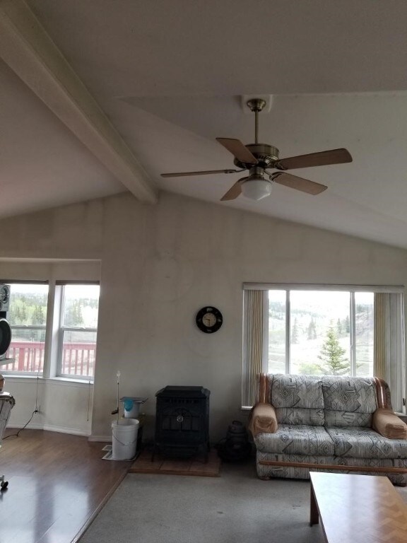 unfurnished living room with wood-type flooring, lofted ceiling with beams, a wood stove, and ceiling fan