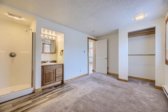 unfurnished bedroom with ensuite bathroom, sink, a textured ceiling, baseboard heating, and a closet