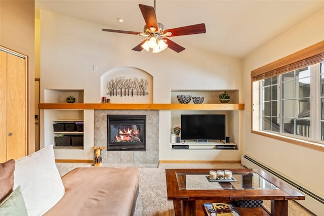 living area with built in features, a ceiling fan, a tiled fireplace, carpet, and a baseboard heating unit