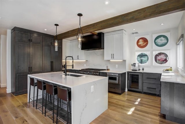 kitchen featuring backsplash, a kitchen island with sink, sink, beam ceiling, and wine cooler