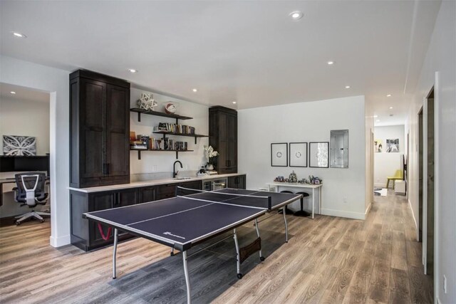 recreation room with electric panel, light hardwood / wood-style flooring, and sink