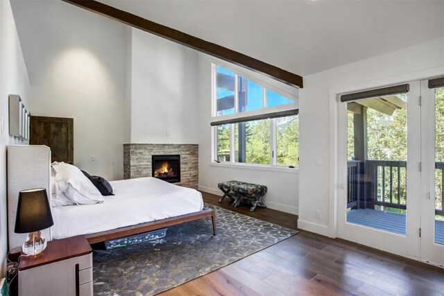 bedroom with access to exterior, a stone fireplace, dark wood-type flooring, and vaulted ceiling with beams