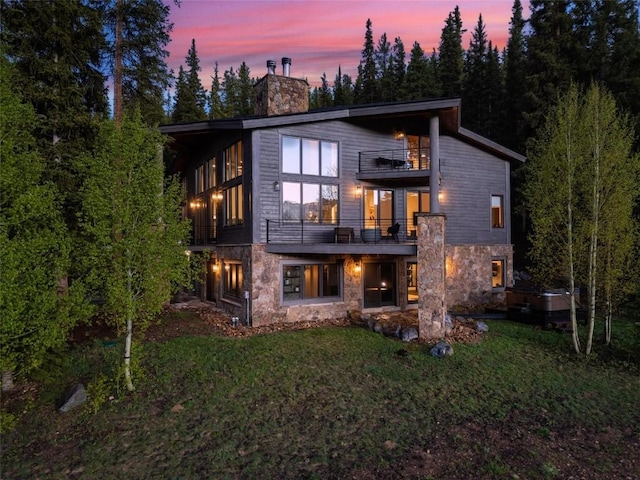 back house at dusk featuring a lawn and a balcony