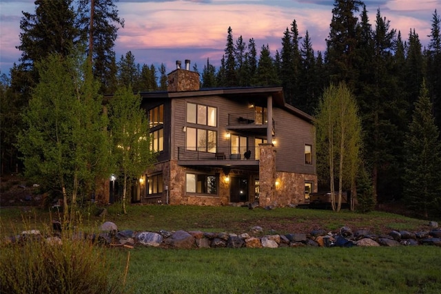 back house at dusk featuring a yard and a balcony