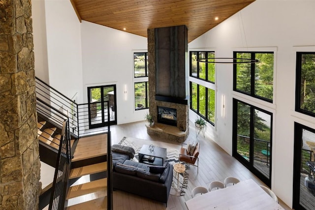 living room featuring a stone fireplace, high vaulted ceiling, wooden ceiling, and light wood-type flooring