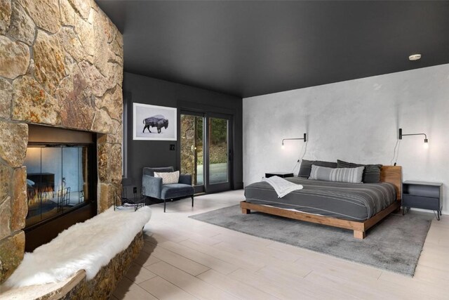 bedroom with access to exterior, a fireplace, and light hardwood / wood-style flooring