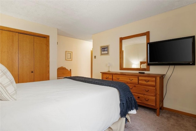 bedroom with a closet, light colored carpet, a textured ceiling, and baseboards