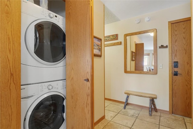 washroom featuring laundry area, stacked washer and clothes dryer, stone finish flooring, and baseboards