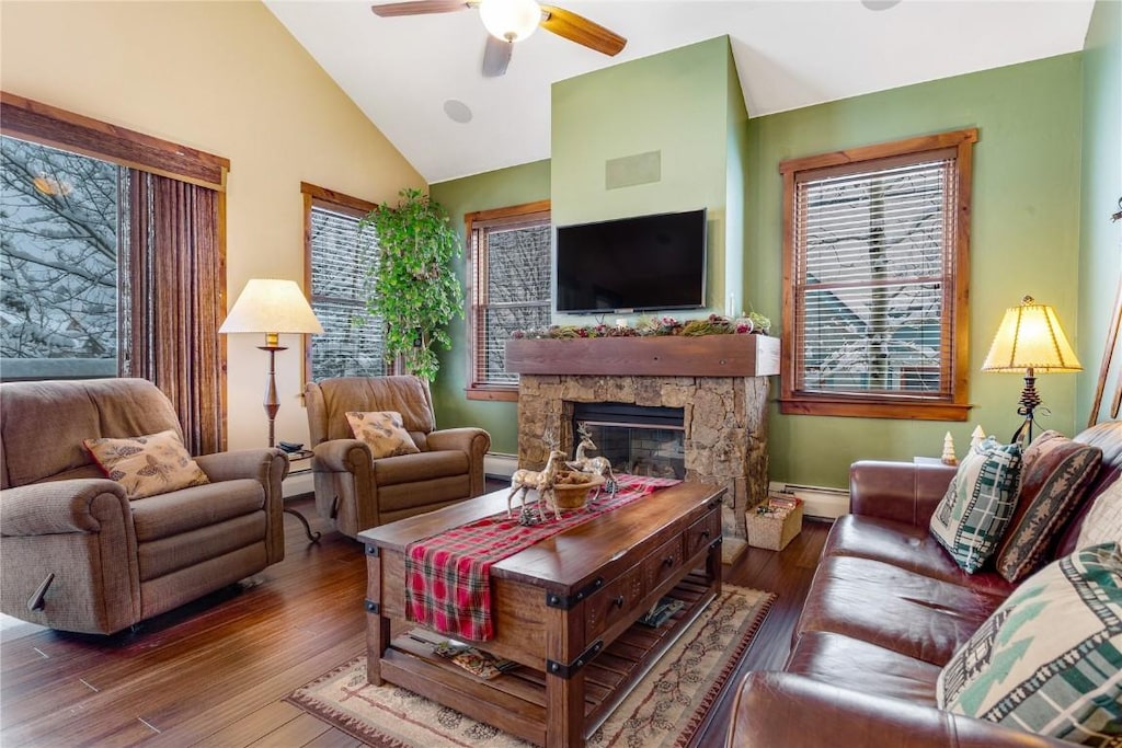 living room featuring vaulted ceiling, hardwood / wood-style flooring, ceiling fan, a fireplace, and a baseboard radiator