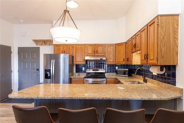 kitchen featuring sink, light stone counters, hanging light fixtures, kitchen peninsula, and stainless steel appliances