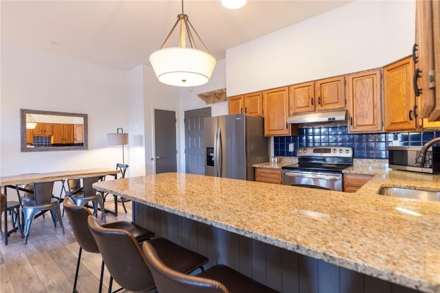 kitchen featuring light stone counters, hanging light fixtures, stainless steel appliances, and a kitchen bar