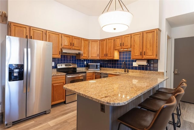 kitchen with sink, a breakfast bar area, light stone counters, hanging light fixtures, and appliances with stainless steel finishes