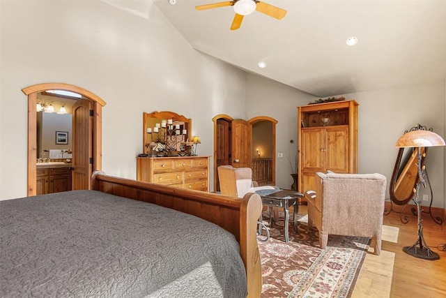 bedroom with recessed lighting, ensuite bathroom, wood finished floors, arched walkways, and high vaulted ceiling