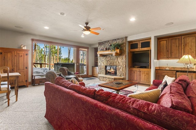 living area with light carpet, a textured ceiling, ceiling fan, and a fireplace