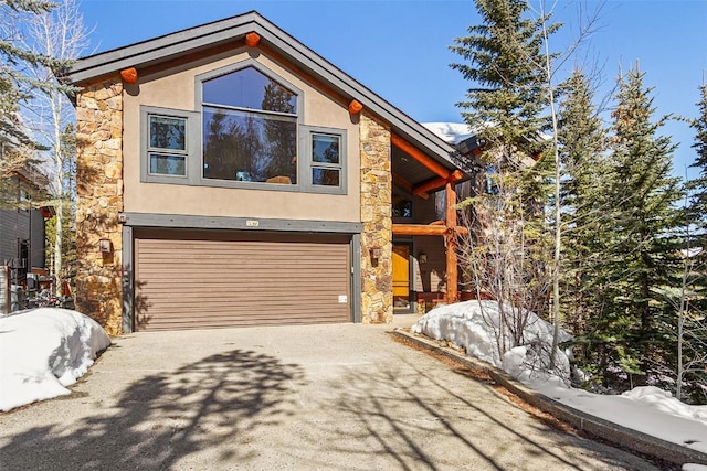 view of front facade featuring a garage, stone siding, driveway, and stucco siding