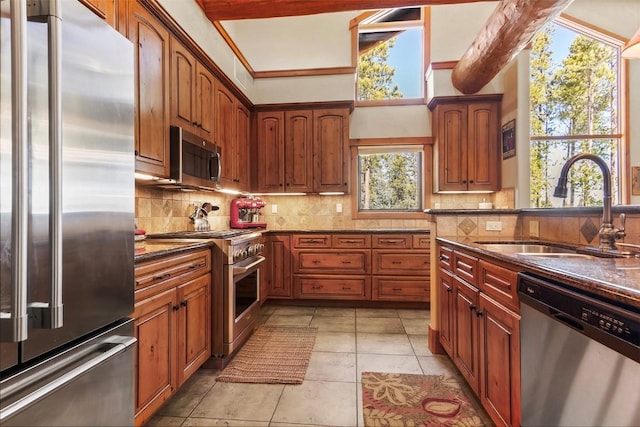 kitchen with a sink, dark stone countertops, light tile patterned flooring, decorative backsplash, and high end appliances