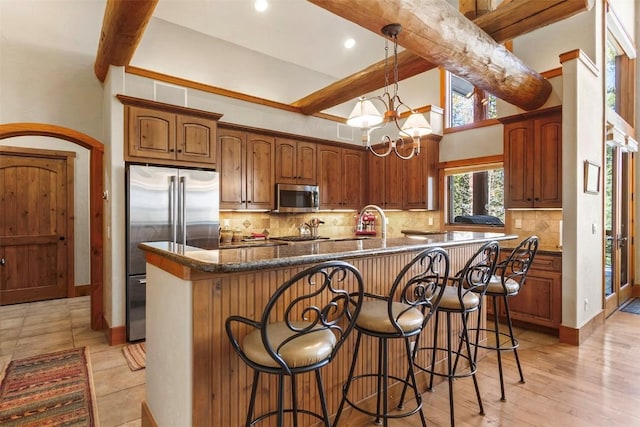 kitchen with tasteful backsplash, beamed ceiling, a kitchen breakfast bar, a notable chandelier, and stainless steel appliances