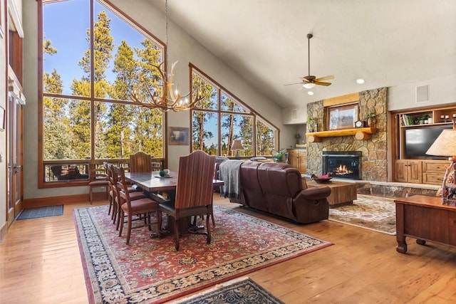 dining area with visible vents, a stone fireplace, a towering ceiling, and hardwood / wood-style flooring