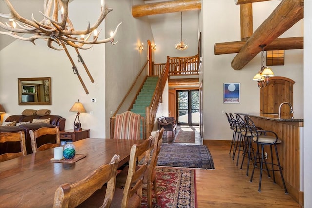 dining space featuring beamed ceiling, stairs, a towering ceiling, wood finished floors, and a notable chandelier