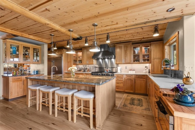 kitchen with pendant lighting, wall chimney exhaust hood, wood ceiling, beamed ceiling, and an island with sink