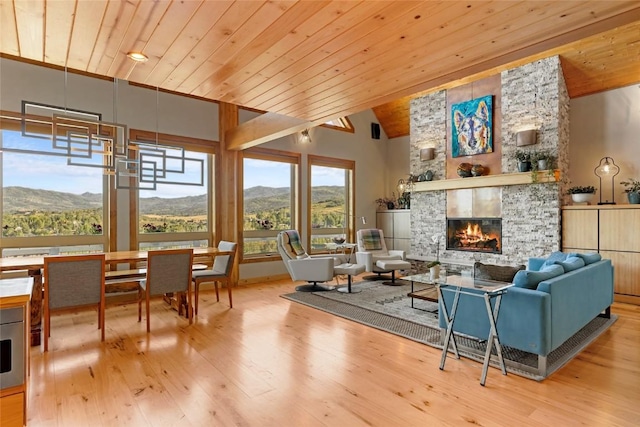 living room featuring light hardwood / wood-style floors, a mountain view, a stone fireplace, high vaulted ceiling, and wooden ceiling