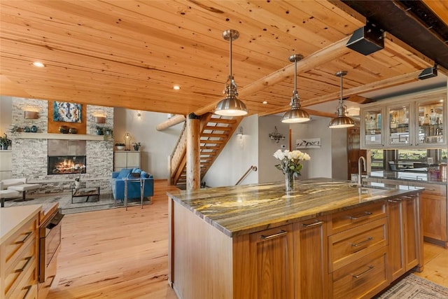 kitchen with decorative light fixtures, light hardwood / wood-style floors, a large island with sink, and a stone fireplace