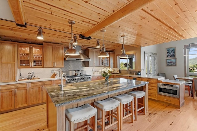 kitchen featuring a center island with sink, wooden ceiling, a breakfast bar area, decorative backsplash, and decorative light fixtures