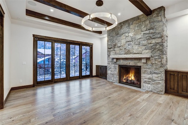 unfurnished living room featuring beamed ceiling, a stone fireplace, and light hardwood / wood-style floors