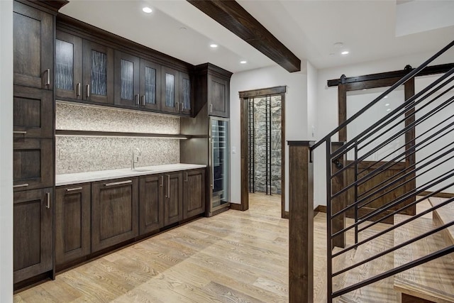 bar featuring dark brown cabinetry, light hardwood / wood-style flooring, a barn door, and beamed ceiling