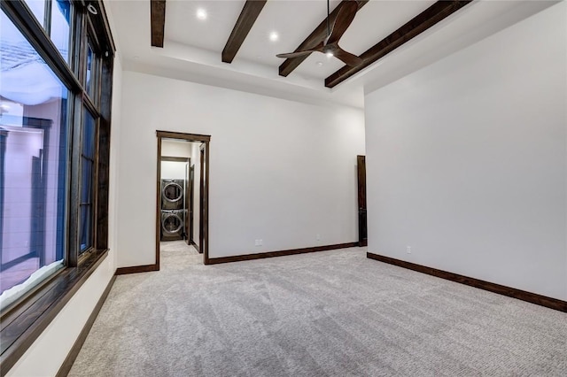 unfurnished room with beam ceiling, light colored carpet, stacked washer and clothes dryer, and ceiling fan