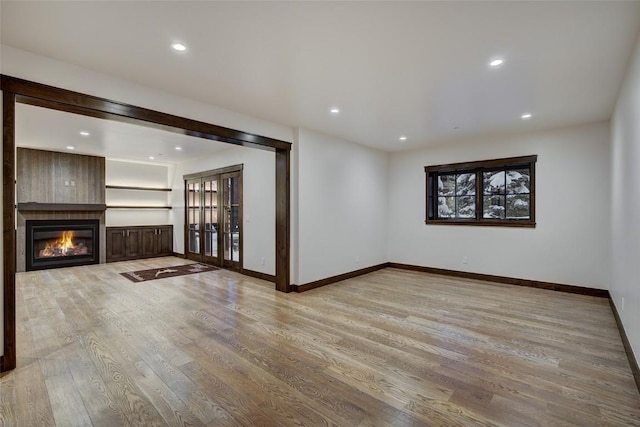 unfurnished living room featuring french doors, a large fireplace, and light hardwood / wood-style floors