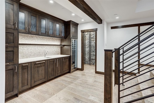 bar featuring beam ceiling, decorative backsplash, dark brown cabinets, and light wood-type flooring