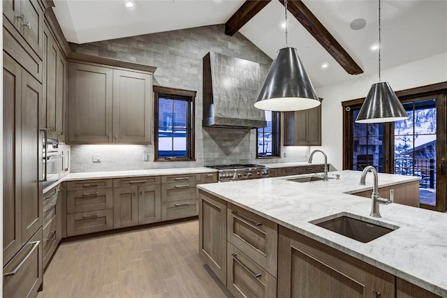 kitchen featuring sink, light stone counters, premium appliances, custom range hood, and decorative light fixtures