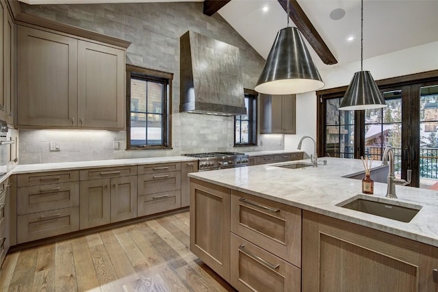 kitchen with sink, vaulted ceiling with beams, light stone countertops, light wood-type flooring, and wall chimney exhaust hood