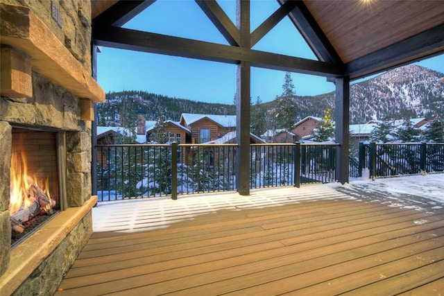 snow covered deck with a mountain view and an outdoor stone fireplace