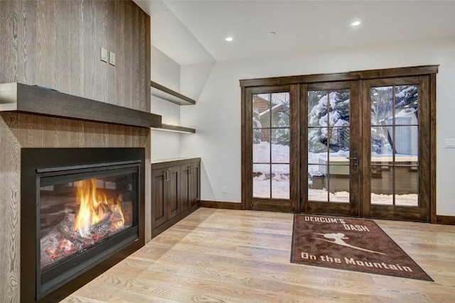 doorway with french doors, a large fireplace, and light wood-type flooring