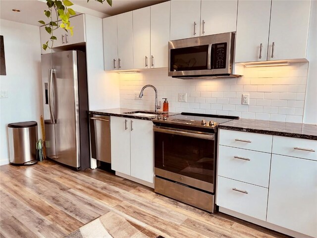 kitchen featuring sink, dark stone countertops, light hardwood / wood-style floors, white cabinets, and appliances with stainless steel finishes