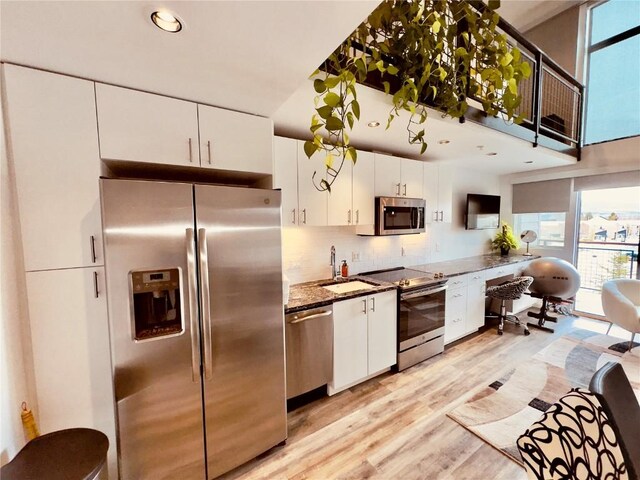 kitchen featuring backsplash, dark stone counters, stainless steel appliances, sink, and white cabinetry