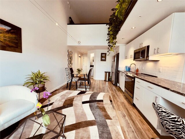 kitchen featuring decorative backsplash, appliances with stainless steel finishes, light wood-type flooring, dark stone counters, and white cabinetry