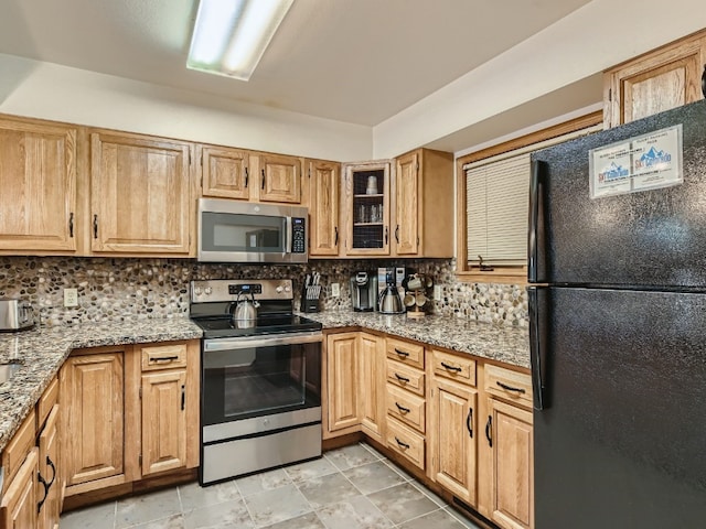 kitchen featuring stainless steel appliances, light stone counters, backsplash, and glass insert cabinets