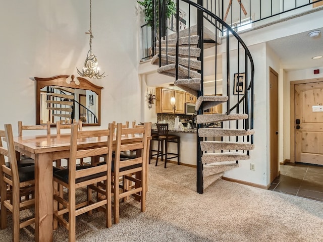 carpeted dining area with a towering ceiling, baseboards, stairway, and a notable chandelier